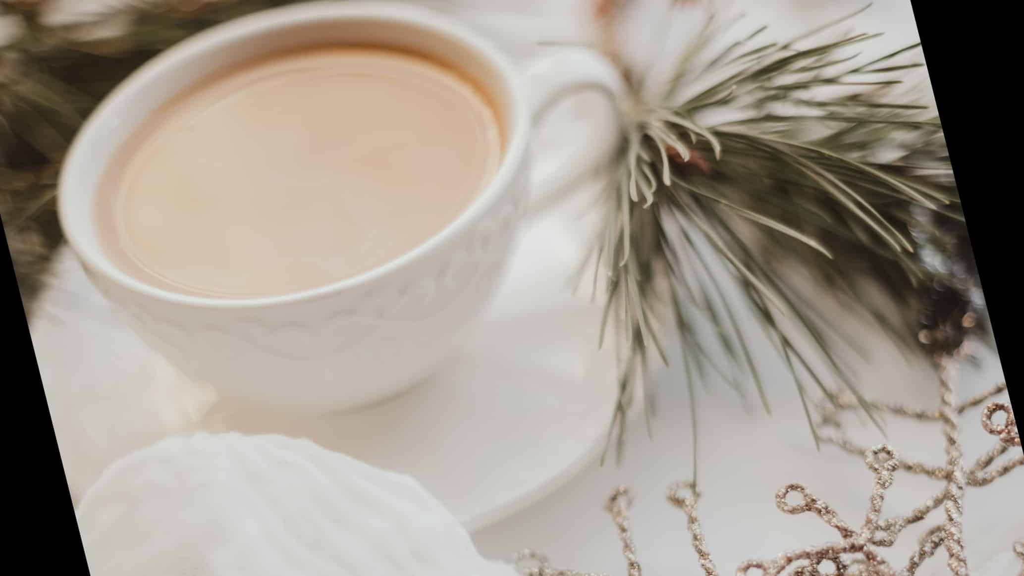 Coffee cup on a coaster sitting on a white tablecloth with a pine branch