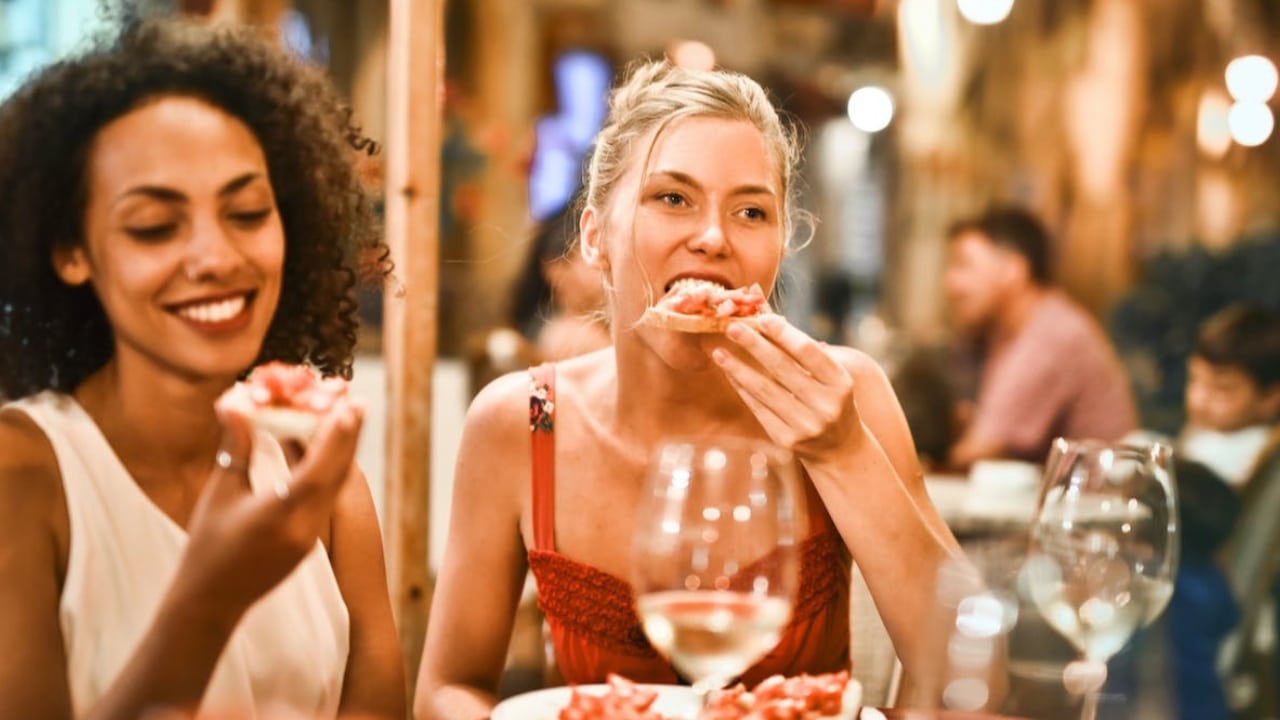 Two friends enjoying open-faced sandwiches with wine glasses.